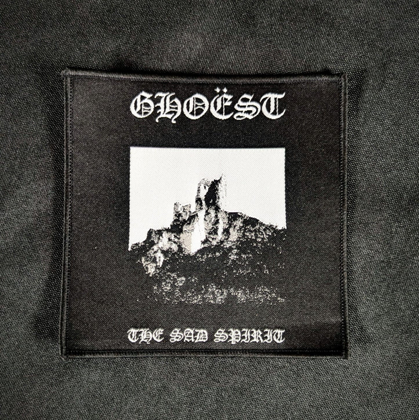 A black and white woven patch with 'GHOÉST' text and an image of a castle on a mountain in the background.