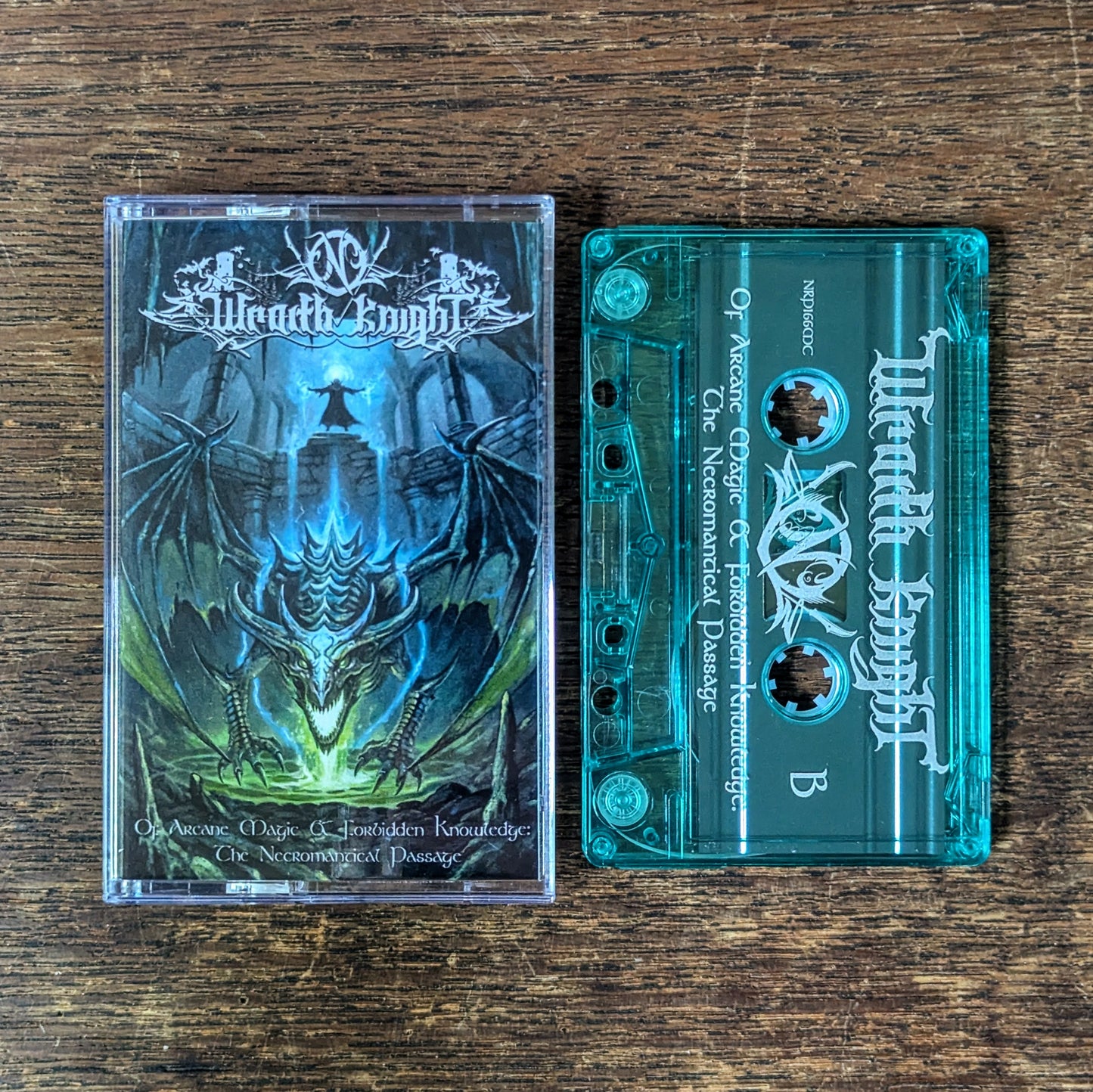 A music release showing a clear plastic cassette tape and its printed jewel case on a dark wood surface. The artwork features a blue and green dragon over a castle.