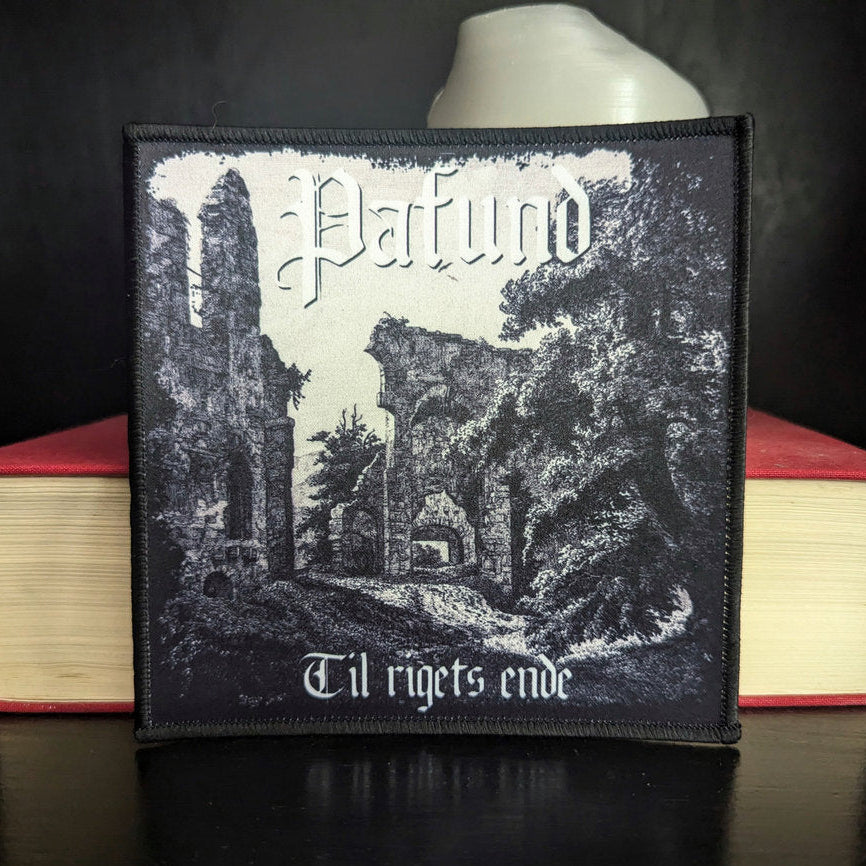 Patch with a black and white design of ruins and text, placed on books with a dark background.