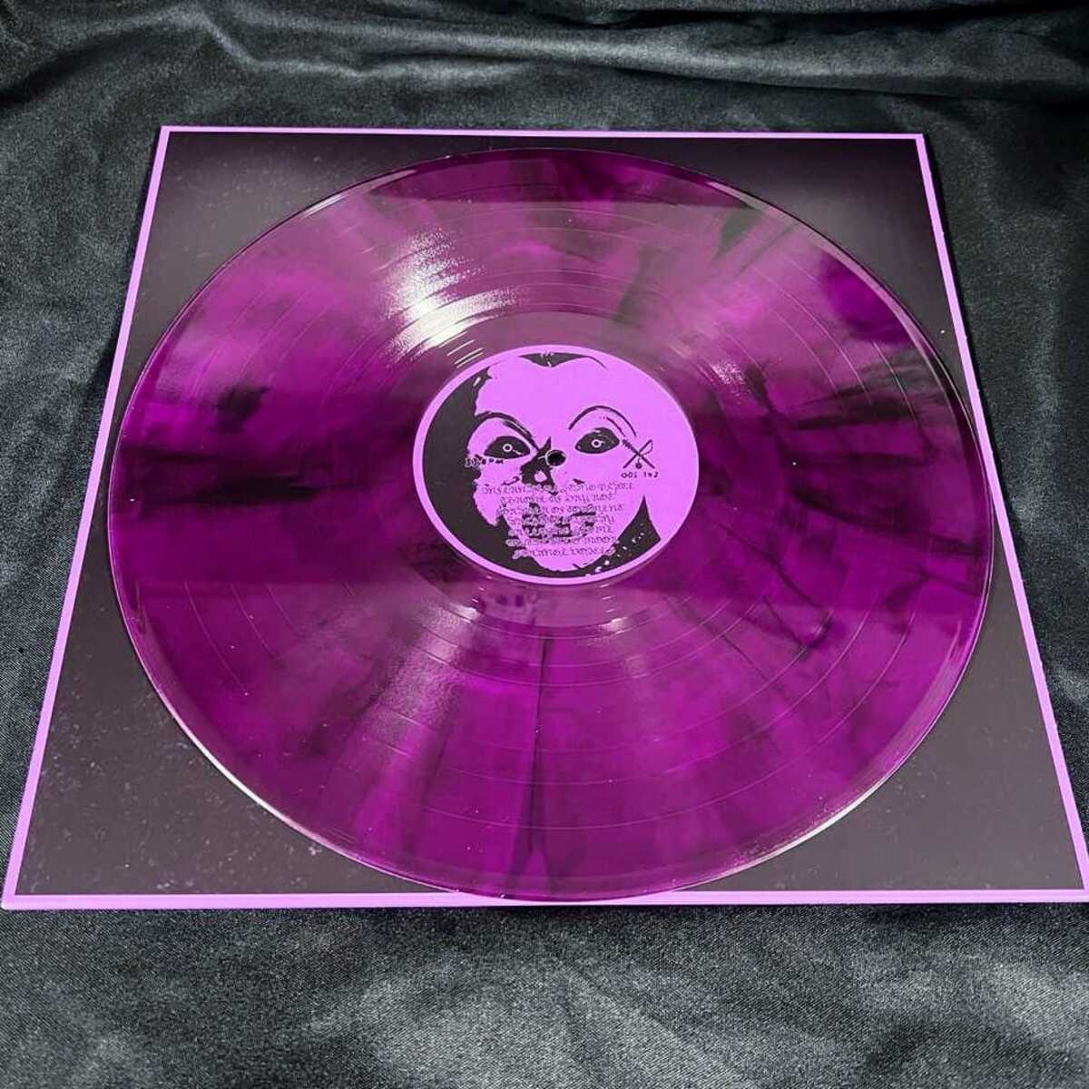 Purple vinyl record with a black and white label on a dark fabric background