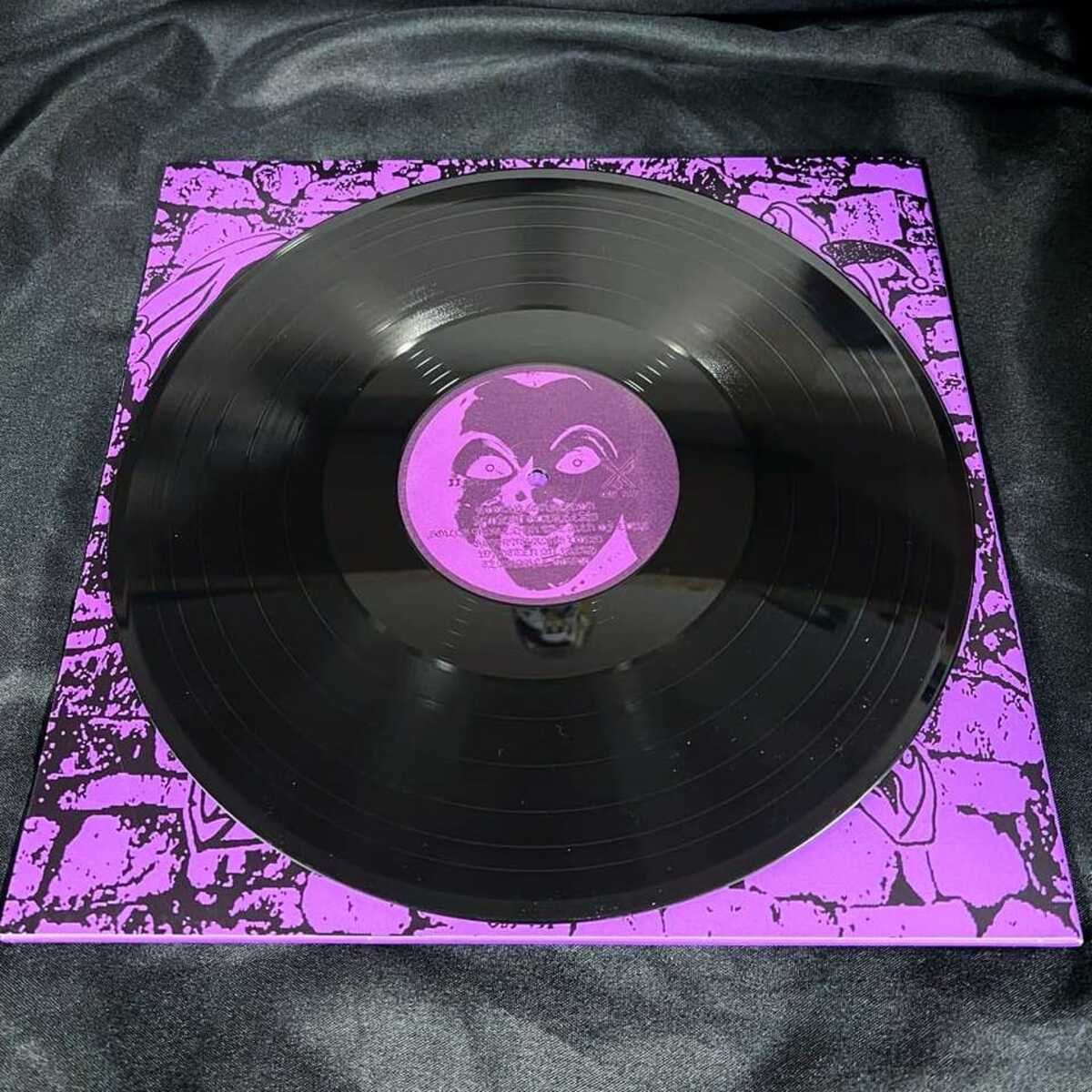 Vinyl record with a purple label on a matching purple and black patterned sleeve against a black background