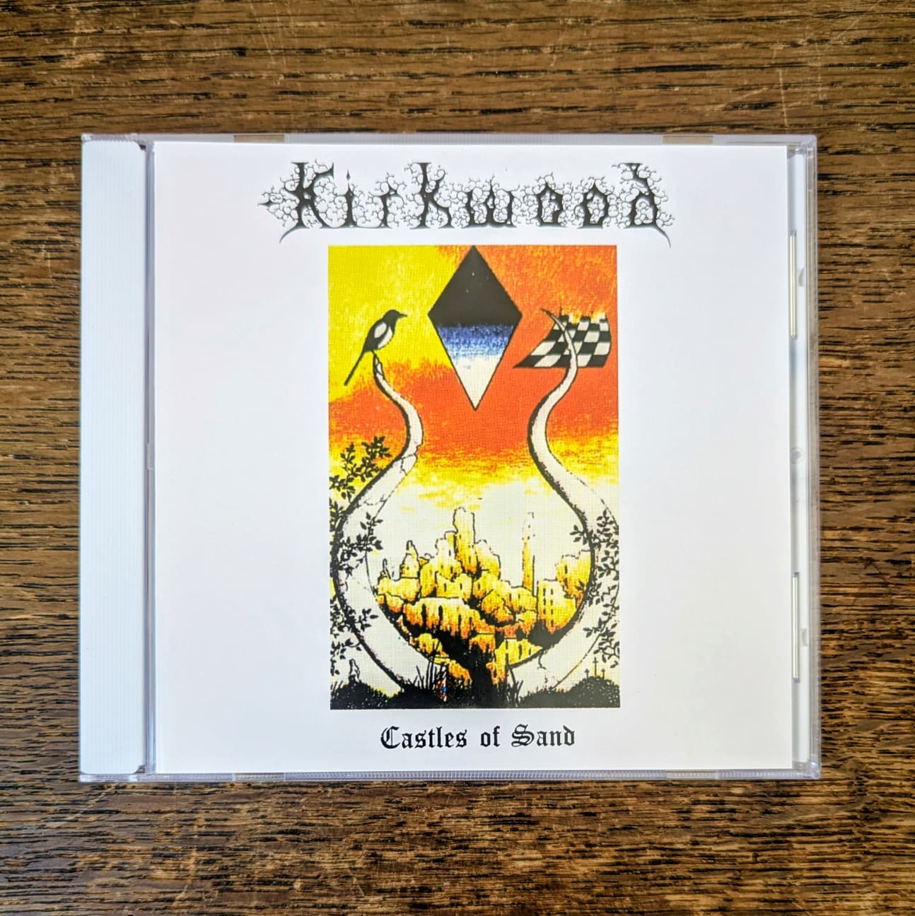 CD cover of 'Castles of Sand' by Kirkwood on a wooden surface